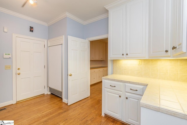 kitchen with light wood finished floors, decorative backsplash, white cabinets, tile countertops, and crown molding