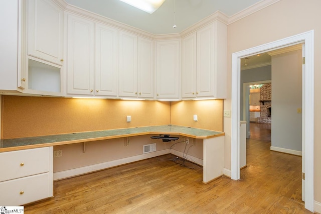 unfurnished office featuring baseboards, visible vents, built in study area, crown molding, and light wood-type flooring