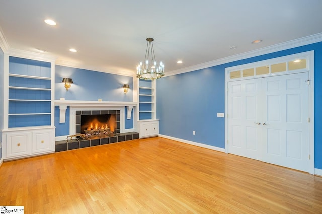 unfurnished living room featuring built in shelves, a tile fireplace, wood finished floors, and crown molding