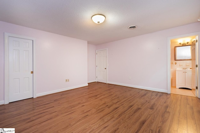 unfurnished room featuring baseboards, a textured ceiling, visible vents, and wood finished floors