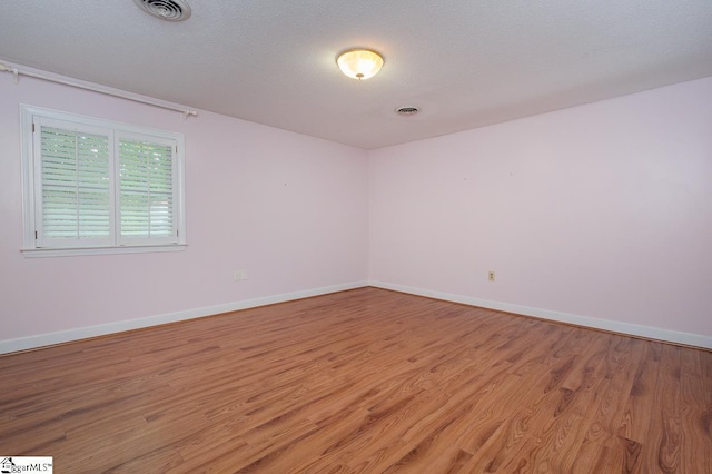 spare room with light wood-type flooring, baseboards, visible vents, and a textured ceiling