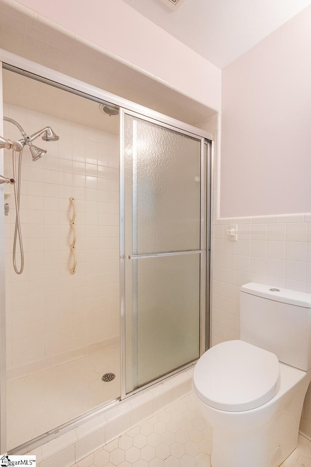 full bathroom with toilet, a wainscoted wall, tile walls, tile patterned floors, and a stall shower