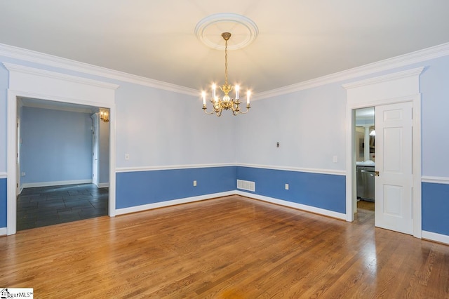 spare room featuring visible vents, an inviting chandelier, ornamental molding, wood finished floors, and baseboards