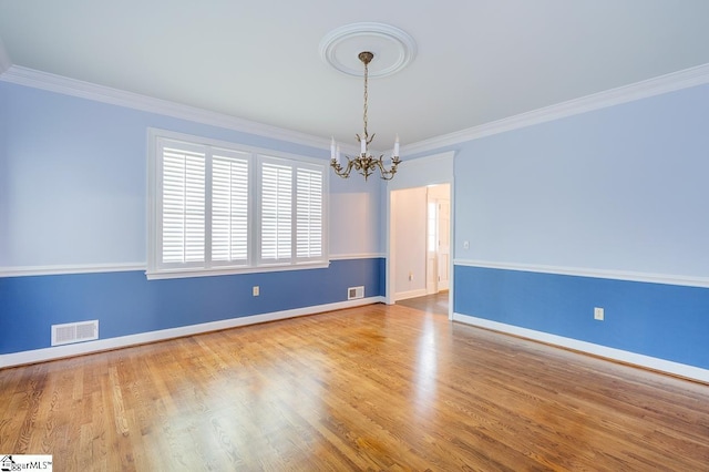 empty room with baseboards, visible vents, ornamental molding, wood finished floors, and a notable chandelier