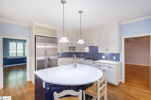 kitchen with stainless steel appliances, a sink, white cabinetry, custom exhaust hood, and crown molding