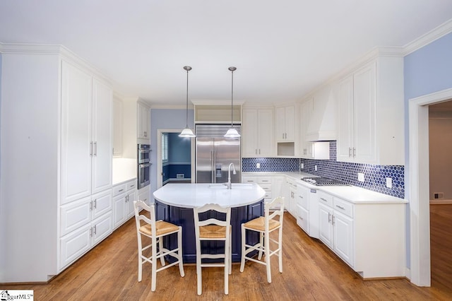 kitchen with stainless steel appliances, a kitchen island with sink, custom exhaust hood, and white cabinetry