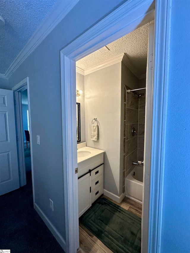 bathroom with a textured ceiling, vanity, hardwood / wood-style floors, ornamental molding, and tiled shower / bath combo