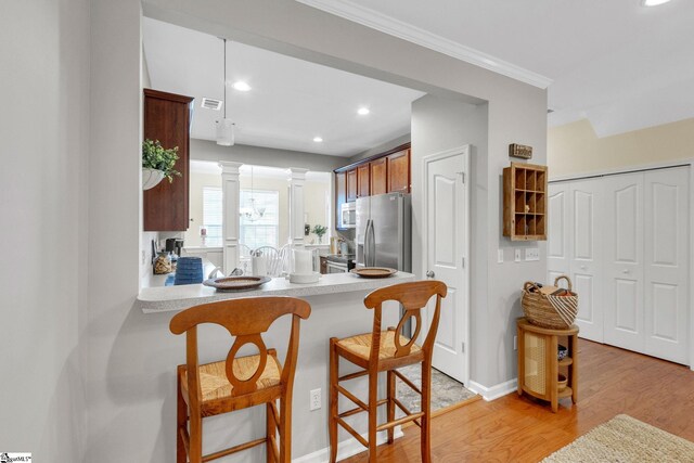 kitchen with stainless steel appliances, light hardwood / wood-style floors, a kitchen bar, ornate columns, and kitchen peninsula