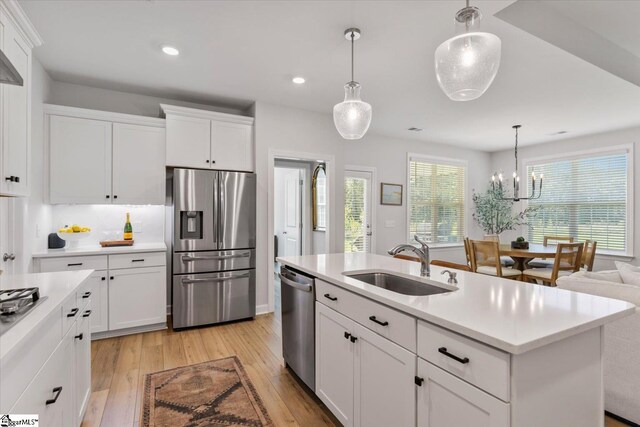 kitchen featuring hanging light fixtures, stainless steel dishwasher, an island with sink, and white cabinets