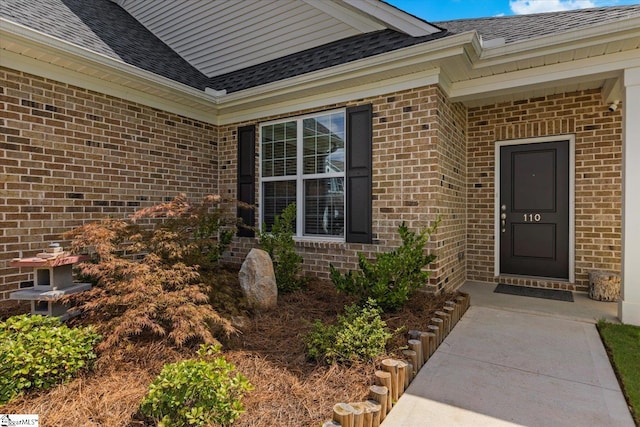 entrance to property featuring a shingled roof and brick siding