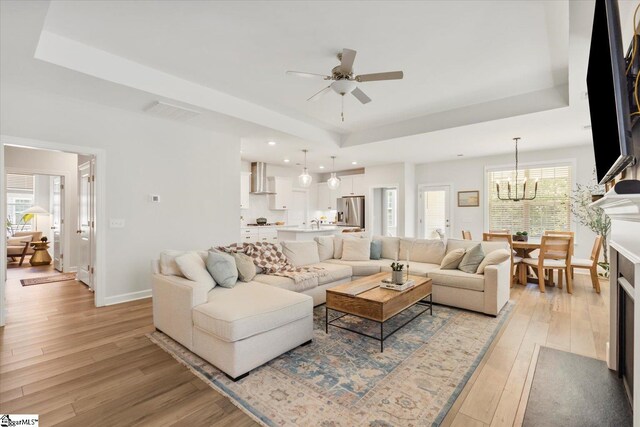 living room featuring ceiling fan with notable chandelier, a tray ceiling, and light hardwood / wood-style floors