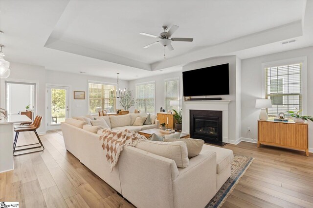 living room featuring ceiling fan with notable chandelier, a raised ceiling, and hardwood / wood-style floors