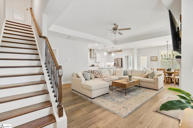 living room featuring light wood-type flooring, a tray ceiling, and ceiling fan