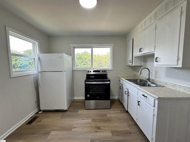 kitchen with a sink, white cabinets, light countertops, freestanding refrigerator, and stainless steel electric stove