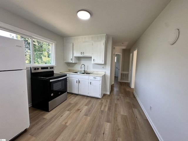 kitchen featuring light countertops, freestanding refrigerator, white cabinetry, a sink, and stainless steel range with electric stovetop