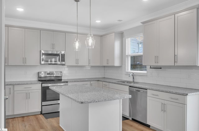 kitchen with a sink, a kitchen island, crown molding, hanging light fixtures, and appliances with stainless steel finishes