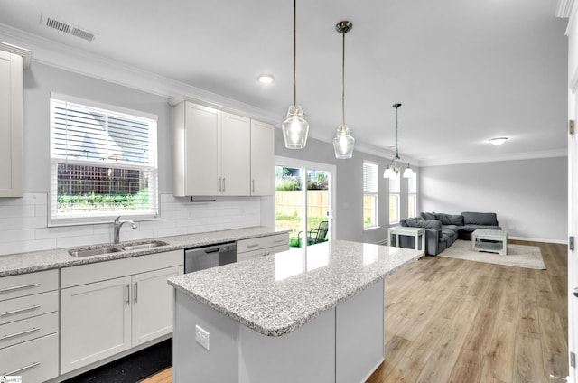 kitchen featuring dishwasher, visible vents, a sink, crown molding, and a center island