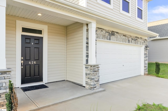 view of exterior entry featuring an attached garage, stone siding, and concrete driveway