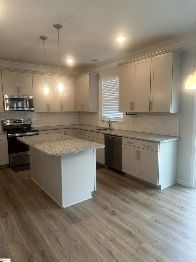 kitchen with stainless steel appliances, decorative light fixtures, decorative backsplash, hardwood / wood-style floors, and a kitchen island