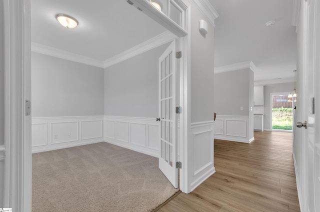 corridor with wainscoting, a decorative wall, crown molding, and light wood-style floors
