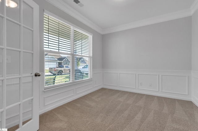 unfurnished room with a wainscoted wall, light colored carpet, a wealth of natural light, and ornamental molding