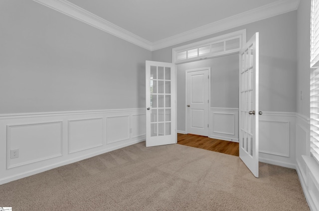 unfurnished room with ornamental molding, french doors, a decorative wall, wainscoting, and carpet flooring