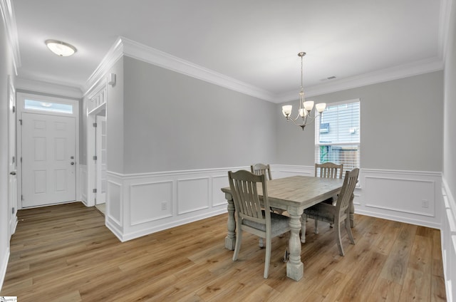 dining room with a decorative wall, crown molding, wainscoting, a chandelier, and light wood finished floors