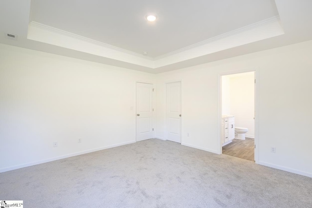 unfurnished bedroom with ensuite bathroom, light colored carpet, crown molding, and a tray ceiling