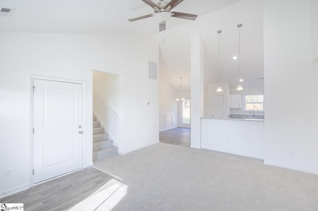 unfurnished living room with ceiling fan with notable chandelier, light colored carpet, and high vaulted ceiling