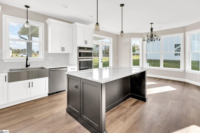 kitchen with sink, a center island, white cabinetry, appliances with stainless steel finishes, and light stone counters