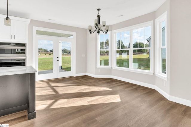 unfurnished dining area featuring an inviting chandelier, plenty of natural light, and hardwood / wood-style floors