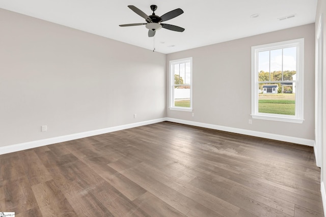 empty room featuring dark wood-type flooring, ceiling fan, and a healthy amount of sunlight