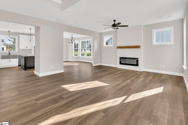 unfurnished living room with wood-type flooring, ceiling fan with notable chandelier, and plenty of natural light