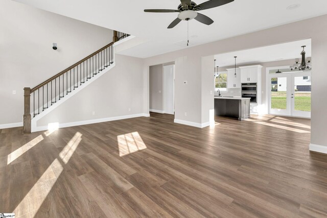 unfurnished living room featuring sink, dark wood-type flooring, and ceiling fan with notable chandelier