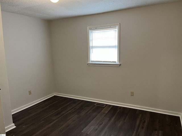 empty room with a textured ceiling, dark wood-type flooring, visible vents, and baseboards