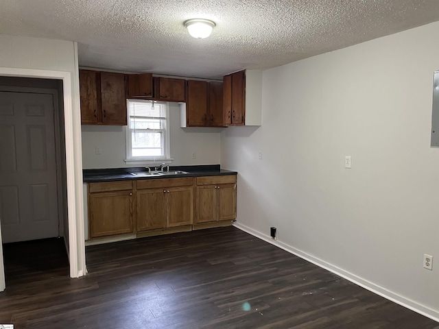 kitchen featuring baseboards, dark countertops, dark wood-type flooring, a textured ceiling, and a sink