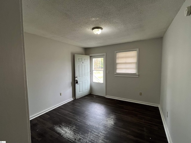 empty room featuring dark wood finished floors, a textured ceiling, and baseboards