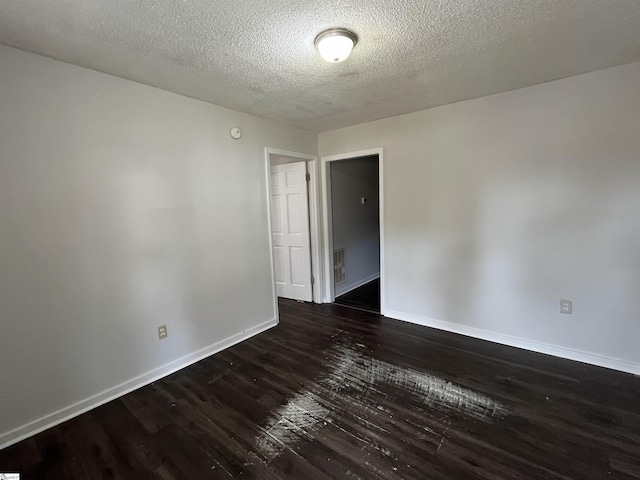 unfurnished room with dark wood-type flooring, visible vents, a textured ceiling, and baseboards