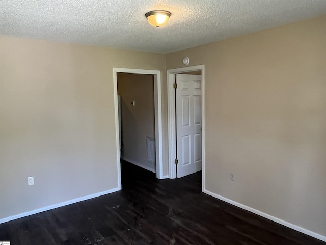 spare room featuring visible vents, a textured ceiling, baseboards, and dark wood-type flooring