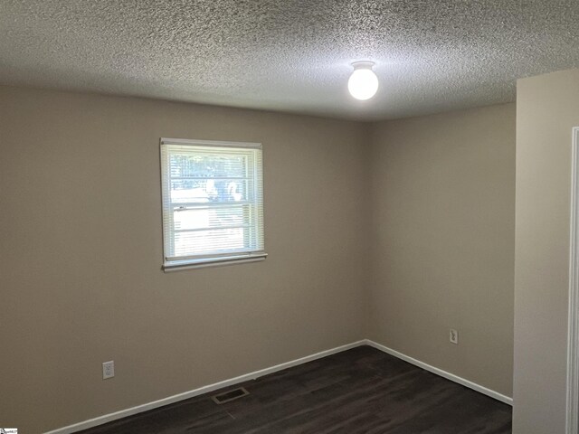 unfurnished room with dark wood-style floors, baseboards, visible vents, and a textured ceiling