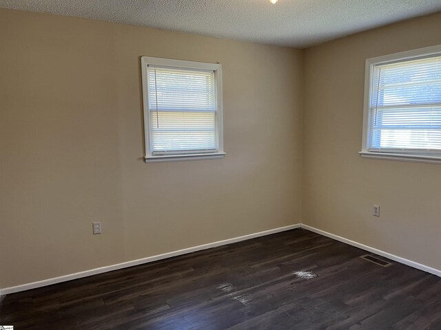 empty room featuring baseboards, a textured ceiling, visible vents, and dark wood-style flooring