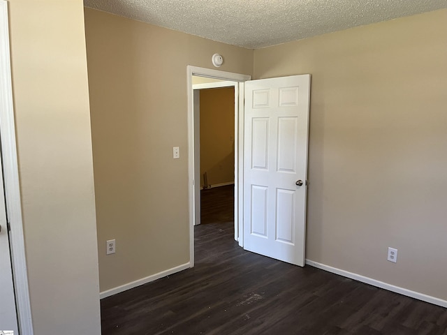 unfurnished room featuring dark wood-style floors, a textured ceiling, and baseboards