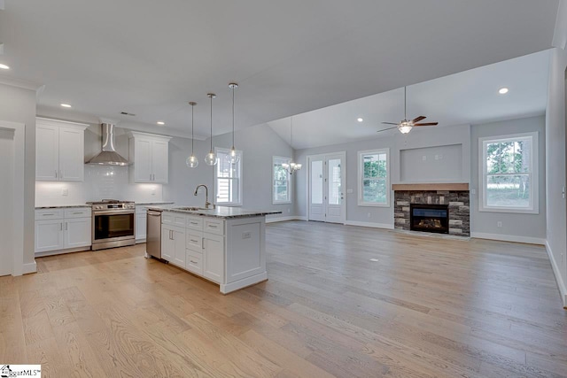 kitchen with stainless steel appliances, wall chimney exhaust hood, plenty of natural light, light wood-type flooring, and a stone fireplace