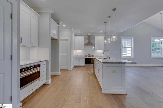 kitchen featuring wall chimney range hood, light wood-type flooring, backsplash, a kitchen island with sink, and stainless steel appliances