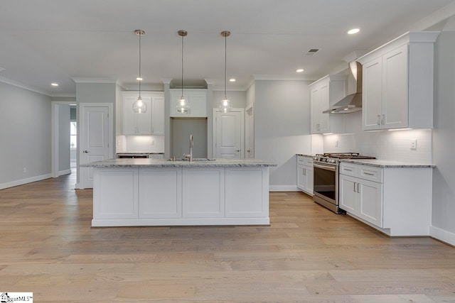 kitchen featuring light wood-type flooring, stainless steel gas range, wall chimney range hood, and white cabinets