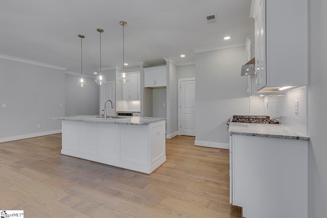 kitchen with light hardwood / wood-style flooring, white cabinetry, tasteful backsplash, sink, and a kitchen island with sink