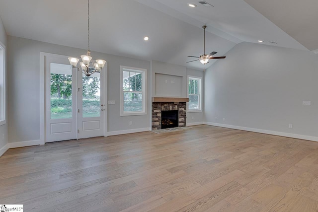 unfurnished living room with light hardwood / wood-style floors, ceiling fan with notable chandelier, a stone fireplace, and lofted ceiling