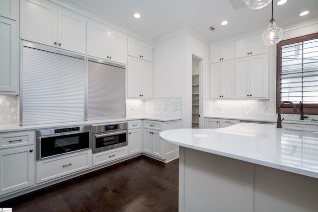 kitchen with light stone countertops, stainless steel oven, pendant lighting, and white cabinets