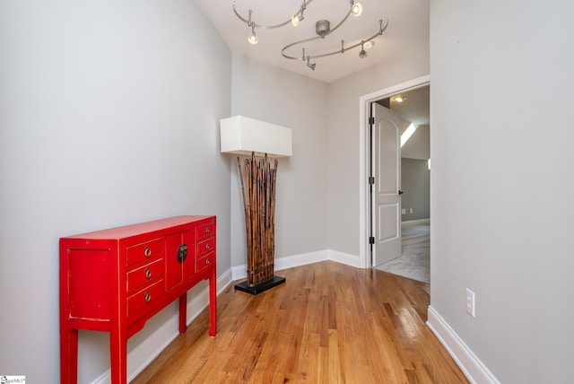 hall featuring rail lighting, light hardwood / wood-style flooring, and a chandelier