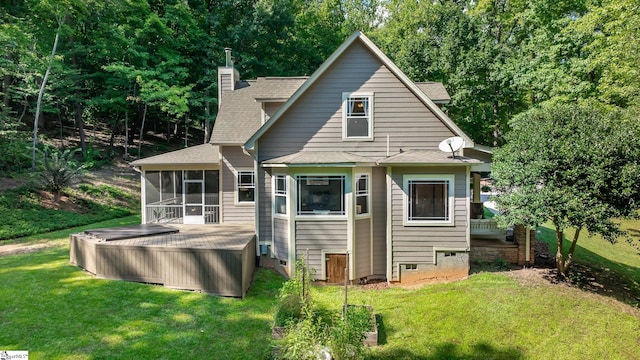 rear view of house with a sunroom, a lawn, and a hot tub